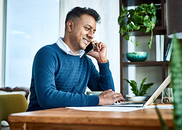 man talking on his cell phone while working on his laptop