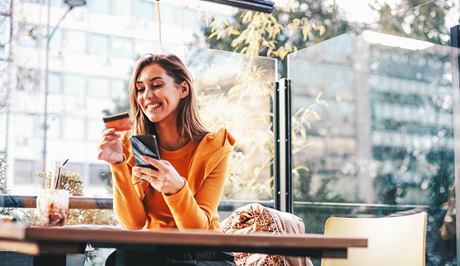 woman holding her phone and debit card at a coffee shop