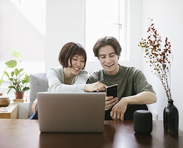 Young couple sitting and smiling at a desk while looking at a laptop
