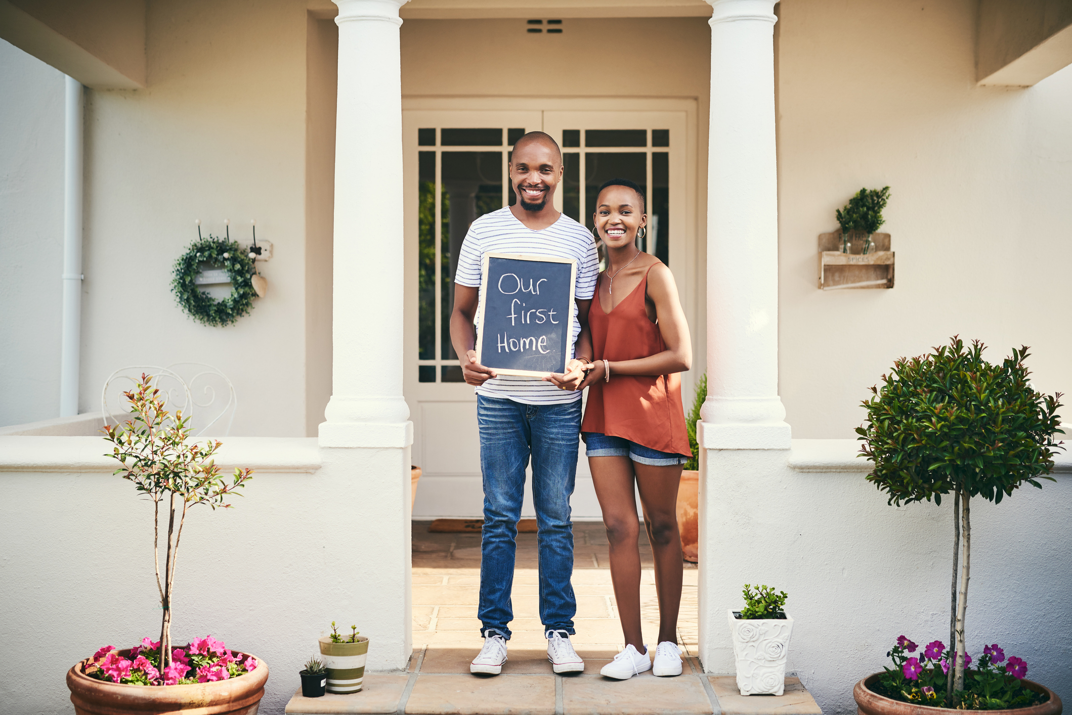 Portrait of a young couple holding a chalkboard with "our first home" written on it