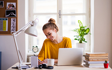 Young woman sitting and smiling at her desk while writing on a notepad